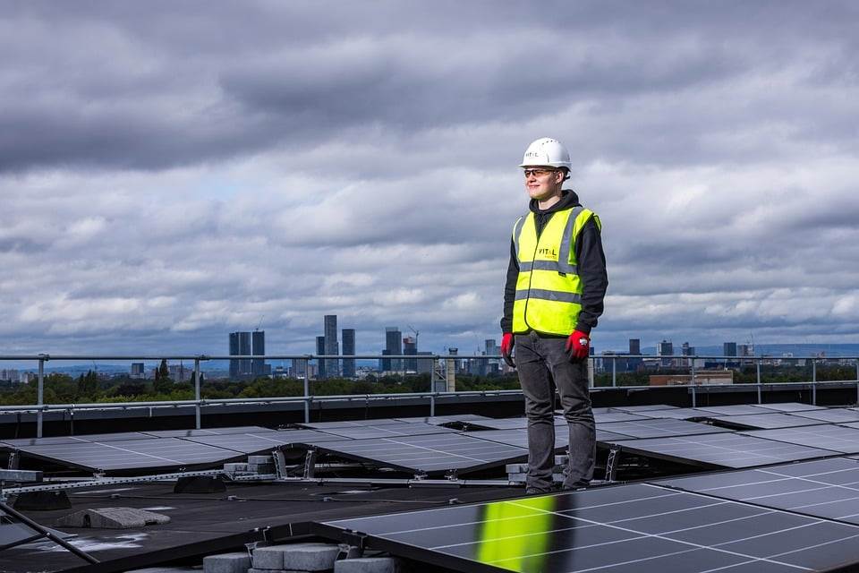 Ingegnere che ispeziona i pannelli solari con un microinverter su un tetto con lo skyline della città sullo sfondo.